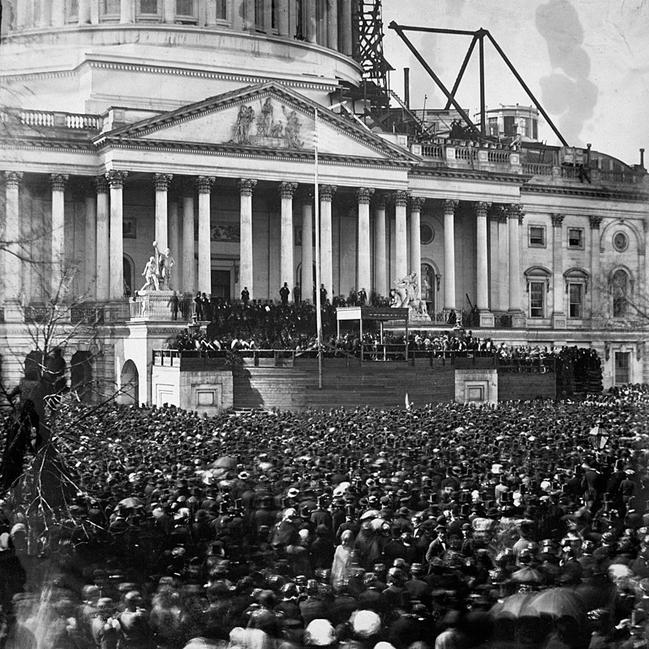 A large crowd in front of a large building with many pillars.